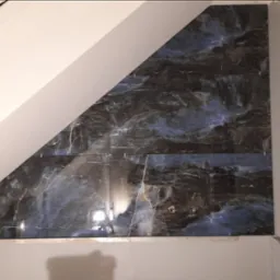 Ukośna ściana poddasza wyłożona płytkami imitującymi ciemny marmur z niebieskimi żyłami, widoczne krzyżyki dystansowe między płytkami.