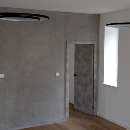 Usługi remontowe malowanie, panele, płytki. - Ściana w szarym kolorze z efektem dekoracyjnym, drewniana podłoga, nowoczesne lampy wiszące w kształcie okręgów, widoczne gniazdka elektryczne i drewniane drzwi.