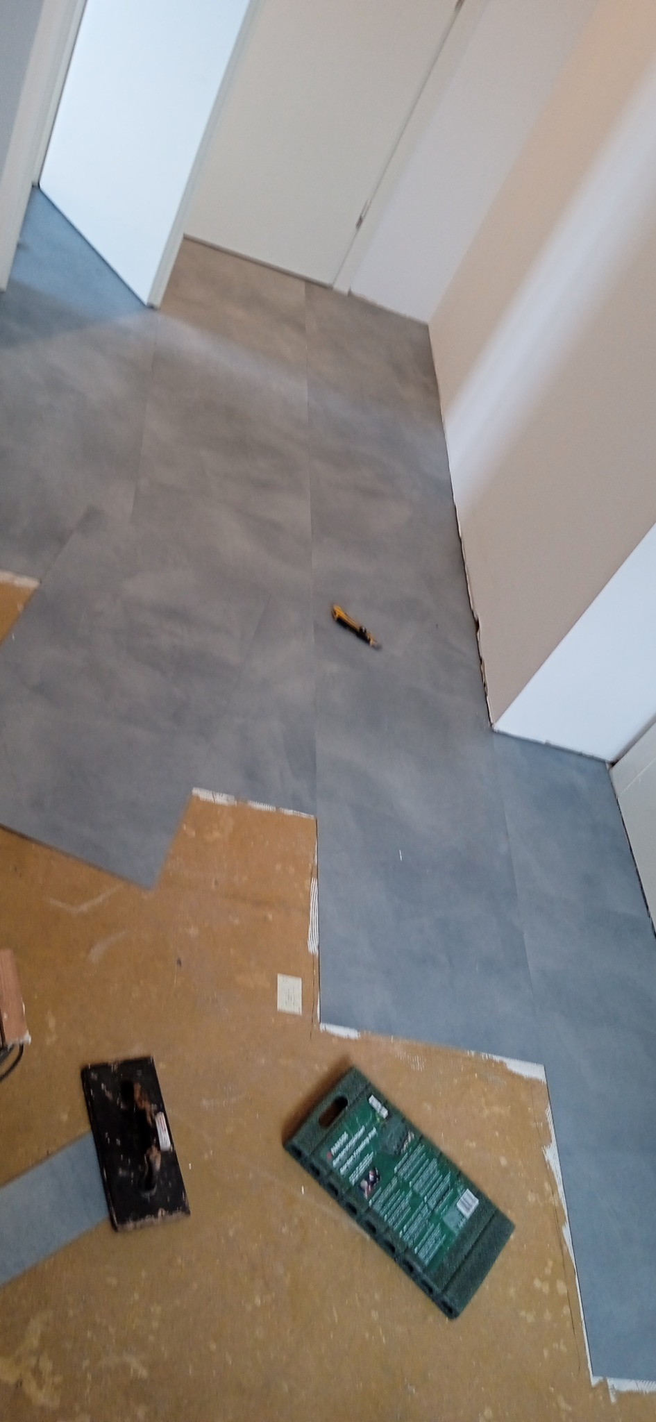 Podczas montażu szarych paneli podłogowych, widoczny fragment podłoża i narzędzia: packa do rozprowadzania kleju i nóż do cięcia paneli.