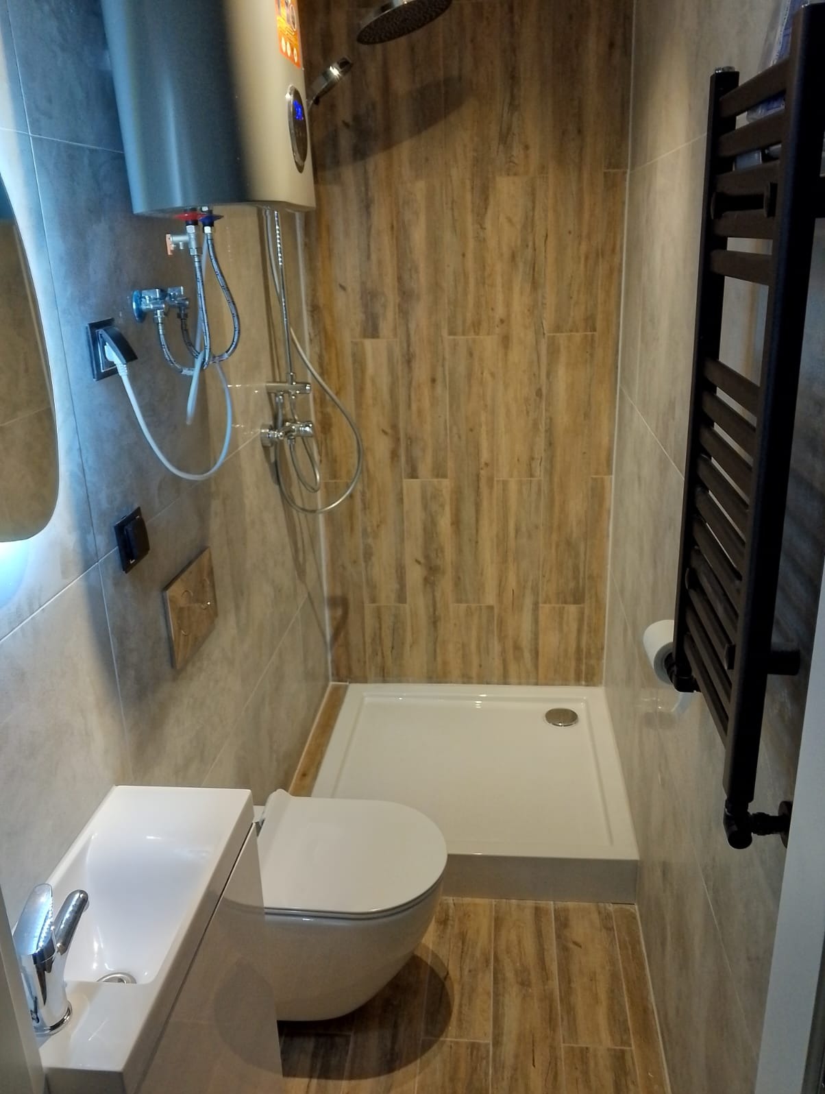 Nowoczesna łazienka z kabiną prysznicową, umywalką nablatową i grzejnikiem drabinkowym. Płytki imitujące drewno na ścianach i podłodze.