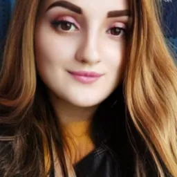 Portret kobiety z brązowymi oczami i włosami w odcieniach brązu i blondu, z delikatnym makijażem w odcieniach różu, ubrana w czarną skórzaną kurtkę z żółtą bluzką pod spodem, na rozmytym tle.