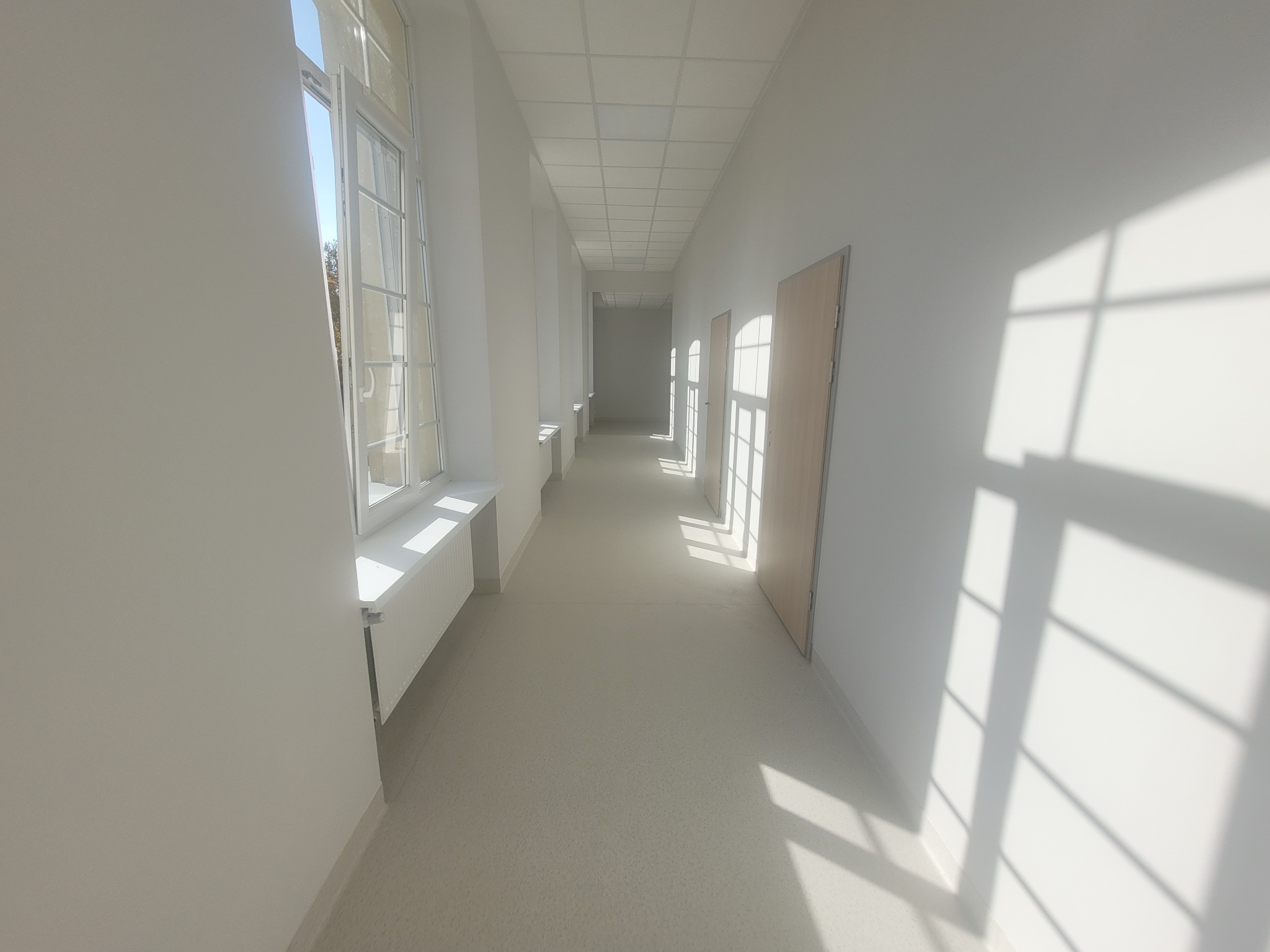 Korytarz biurowy po remoncie w Łodzi, z jasnymi ścianami, panelami sufitowymi i promieniami słońca wpadającymi przez okna.