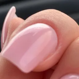 Zbliżenie na palec z delikatnym, różowym manicure hybrydowym o kwadratowym kształcie. Widoczna gładka powierzchnia lakieru i struktura skóry palca.