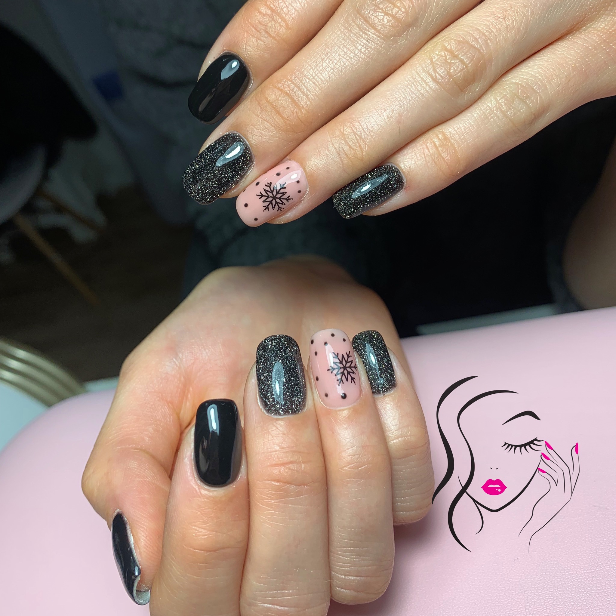 Dłonie z manicure hybrydowym: czarne, brokatowe i różowe paznokcie z motywem śnieżynki na różowym tle z logo salonu kosmetycznego.