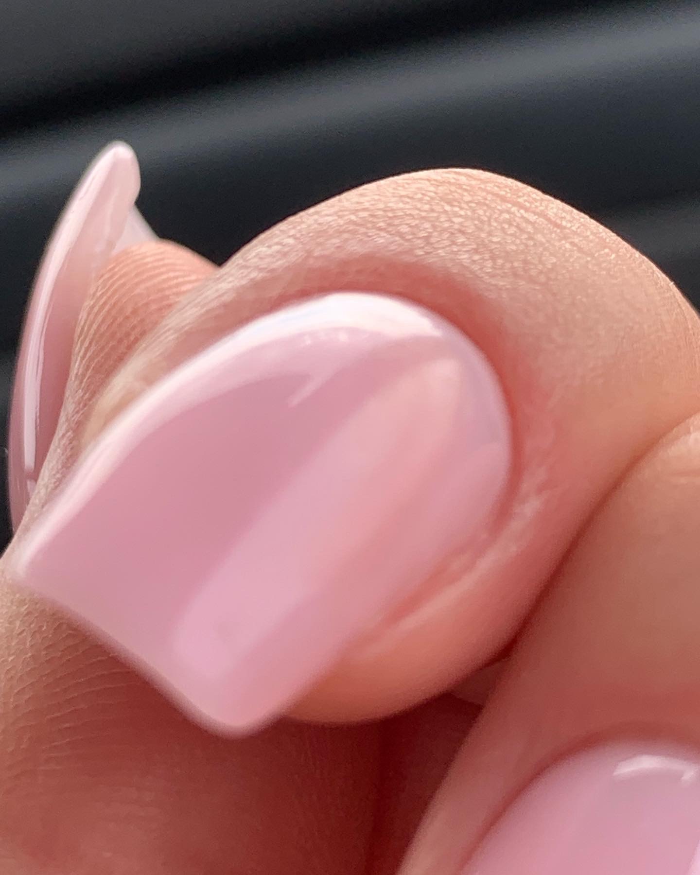 Zbliżenie na palec z delikatnym, różowym manicure hybrydowym o kwadratowym kształcie. Widoczna gładka powierzchnia lakieru i struktura skóry palca.