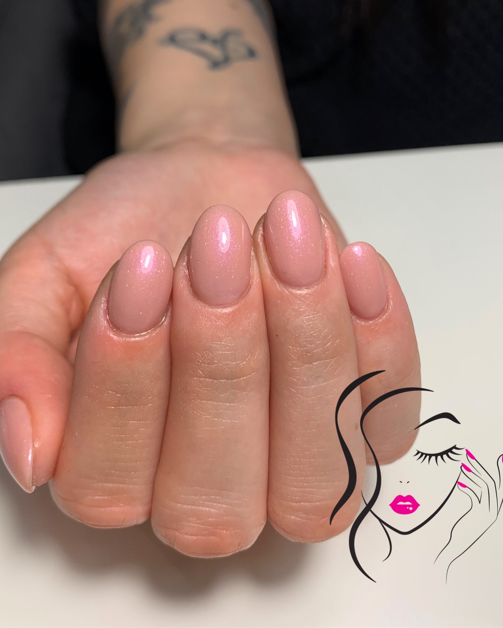 Delikatny, różowy manicure hybrydowy z subtelnym połyskiem na zadbanych dłoniach, prezentowany na białym tle z dodatkiem grafiki przedstawiającej twarz kobiety.