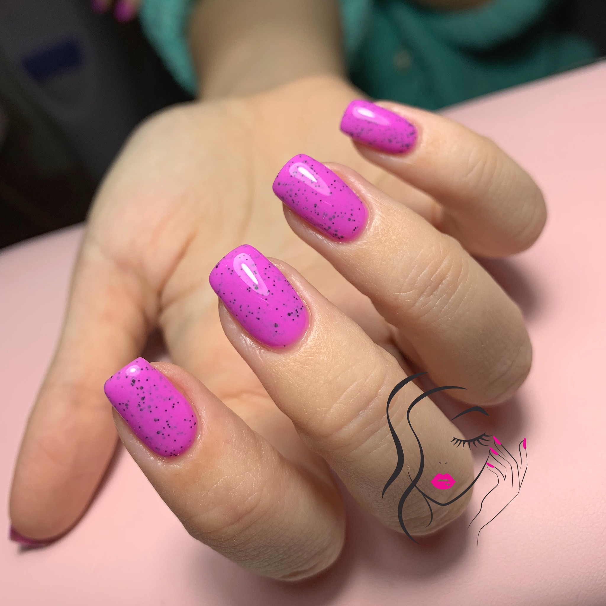 Dłoń z pomalowanymi na różowo paznokciami z czarnymi drobinkami na tle różowego stołu; na dłoni nałożona grafika przedstawiająca twarz kobiety.