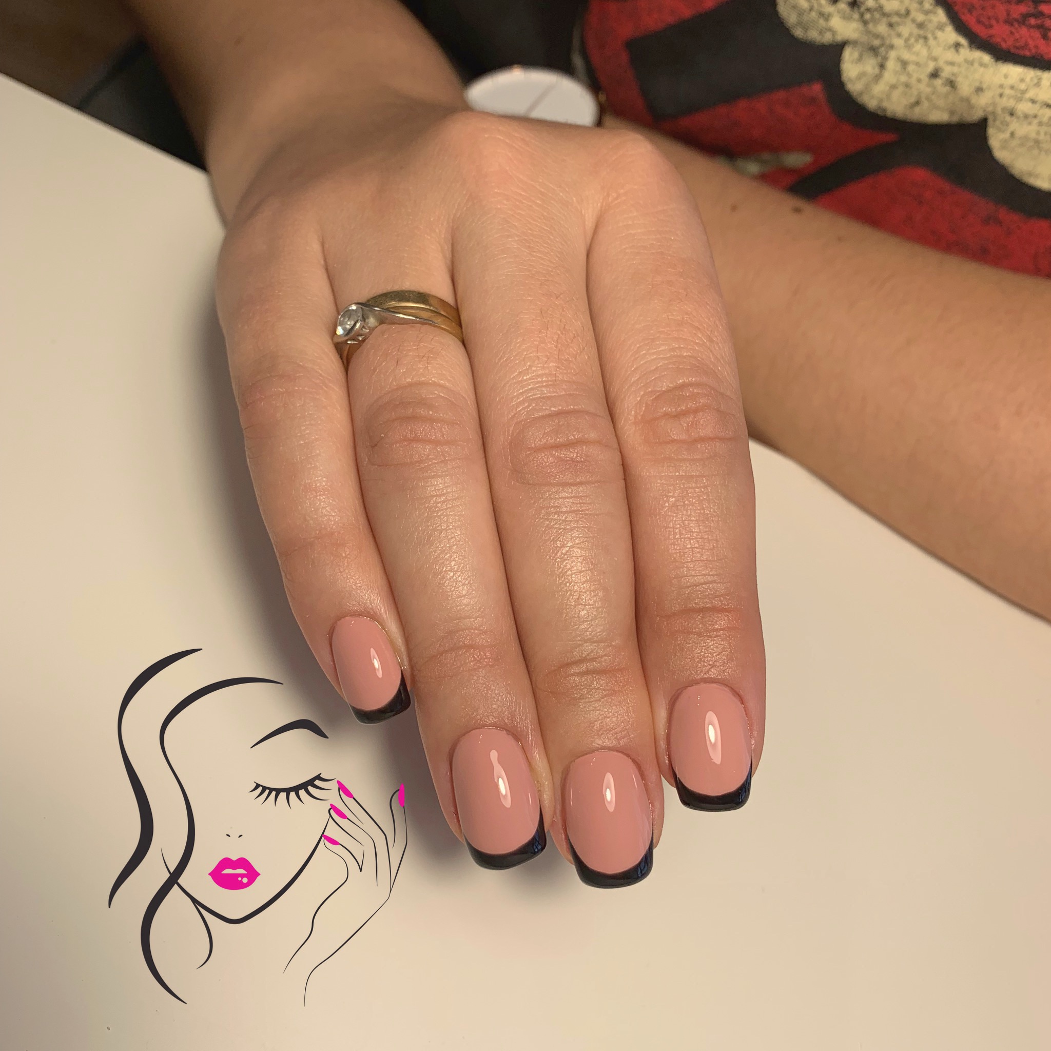 Dłoń z pierścionkiem prezentuje klasyczny manicure francuski z czarną końcówką na tle rysunku kobiety z różowymi ustami i paznokciami.