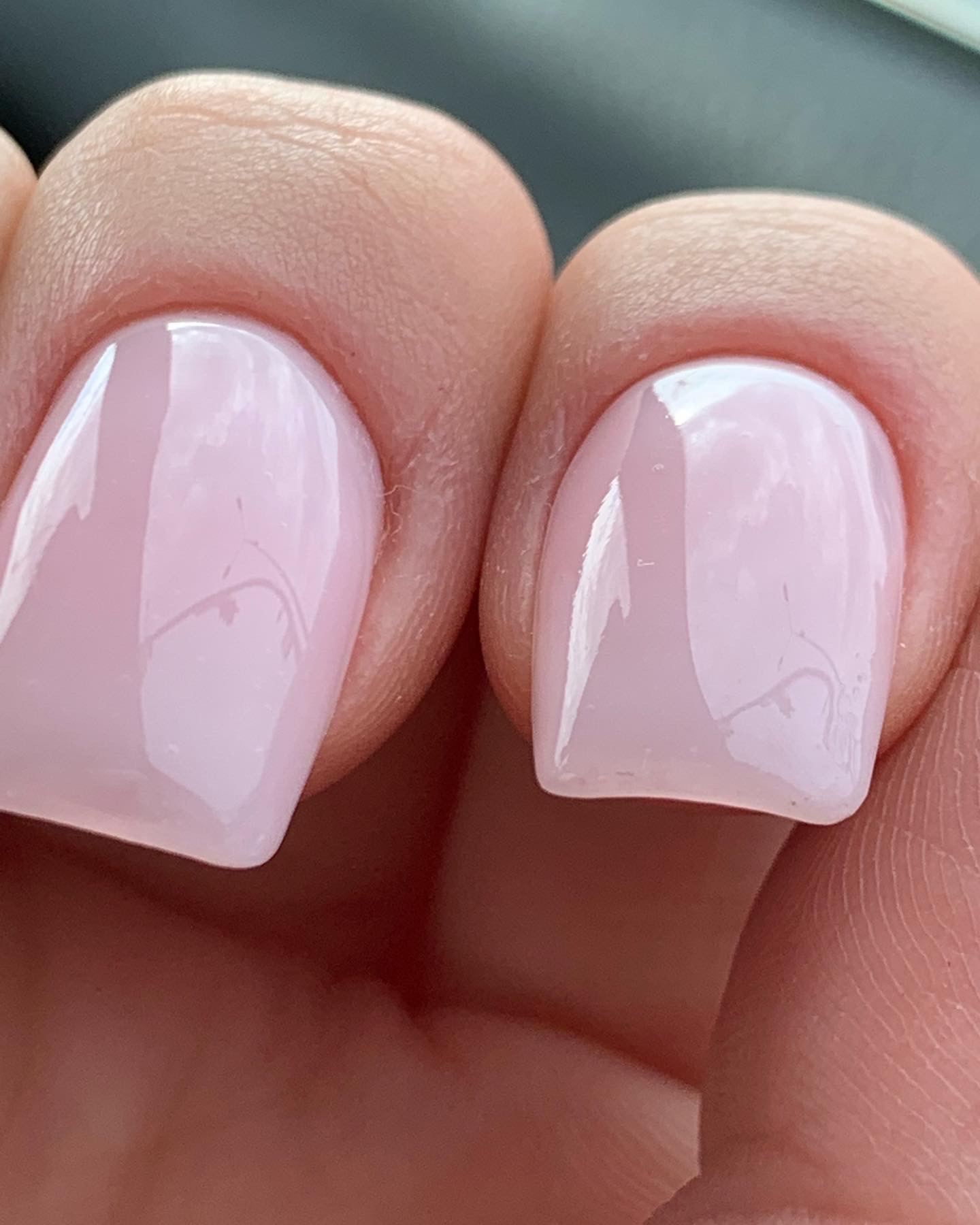 Zbliżenie na dwa paznokcie z kwadratowym kształtem i delikatnym, jasnoróżowym lakierem. Na lakierze widoczne delikatne rysy.