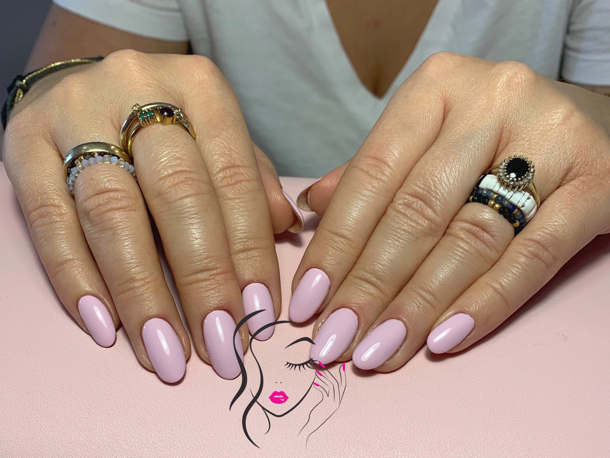 Delikatny, pastelowy róż na migdałowych paznokciach, ozdobione pierścionkami na palcach, na gładkim różowym tle z subtelnym logo salonu kosmetycznego.