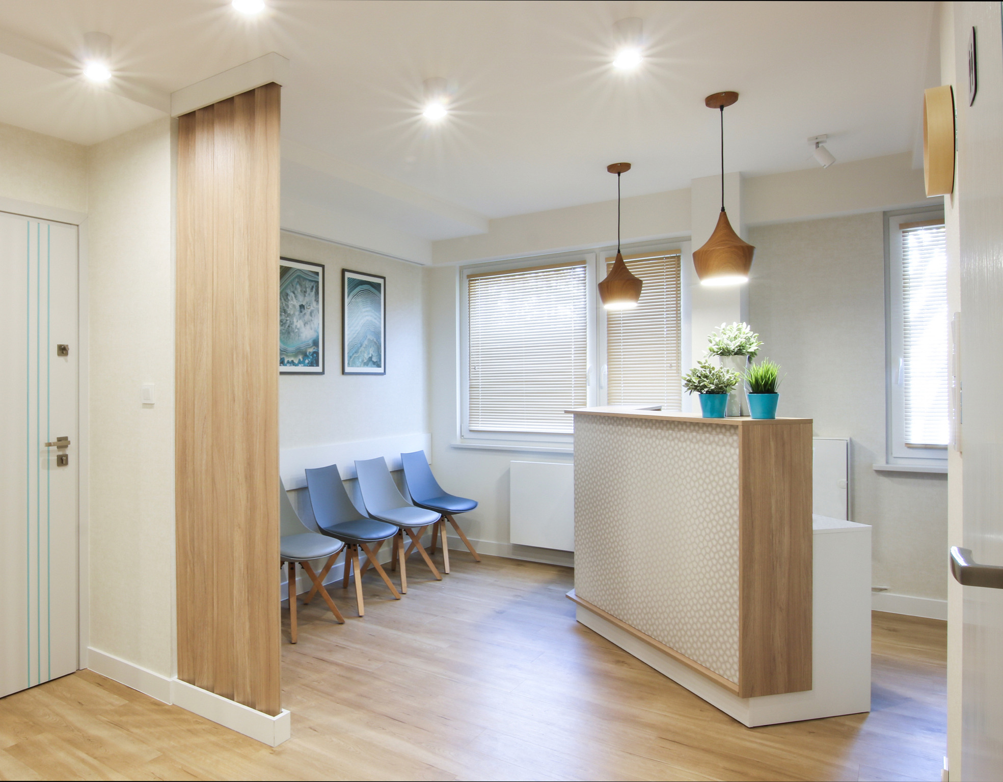 Jasne, minimalistyczne biuro z recepcją, drewnianymi lampami wiszącymi, szarymi krzesłami i abstrakcyjnymi obrazami na ścianie.