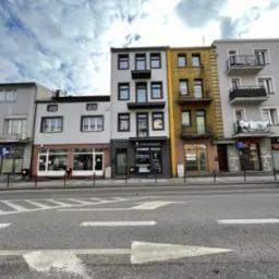 Fasada budynku z nowoczesnymi oknami i drzwiami wejściowymi, widok z poziomu ulicy w pochmurny dzień.