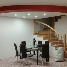 Auri - Jasne wnętrze domu z drewnianymi schodami, stołem jadalnym i pomalowanym na czerwono łukiem sufitowym oraz filarem.