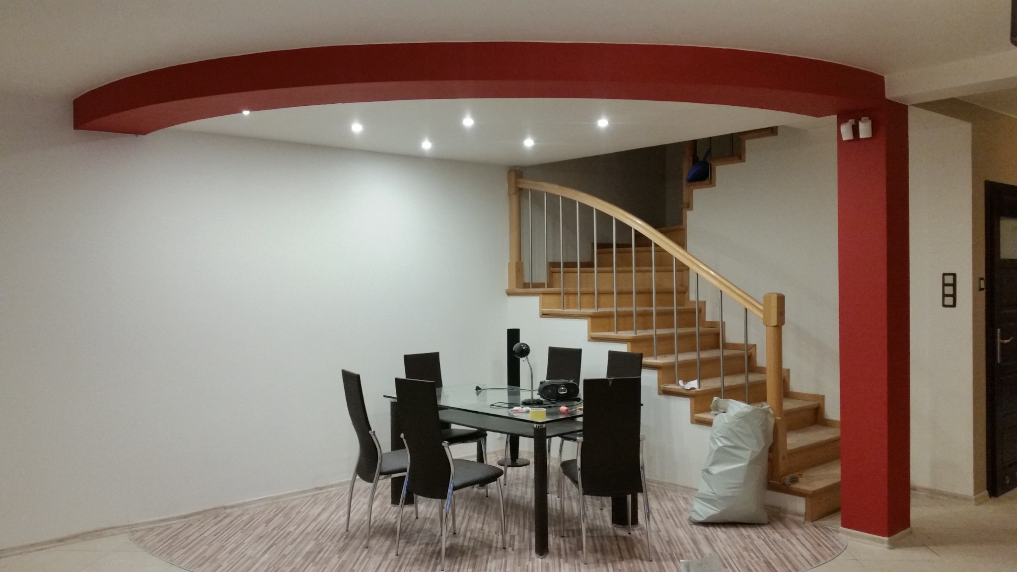 Jasne wnętrze domu z drewnianymi schodami, stołem jadalnym i pomalowanym na czerwono łukiem sufitowym oraz filarem.