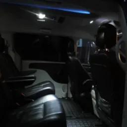 Wnętrze czarnego busa z skórzanymi fotelami, oświetleniem sufitowym i kratkowaną podłogą, widok z otwartych drzwi.