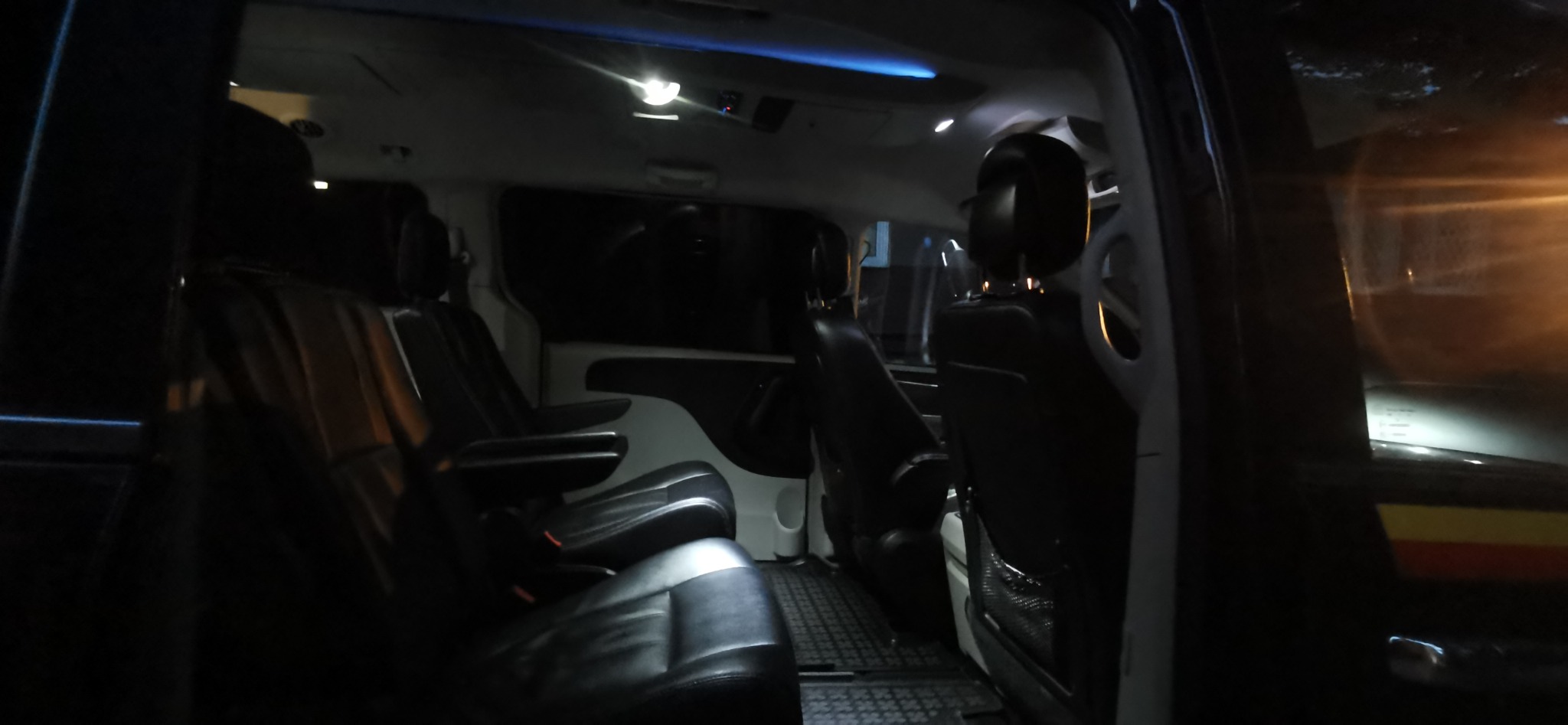 Wnętrze czarnego busa z skórzanymi fotelami, oświetleniem sufitowym i kratkowaną podłogą, widok z otwartych drzwi.