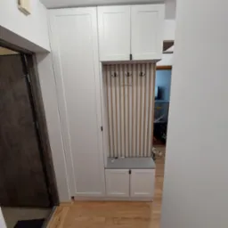 Wnękowa szafa w przedpokoju z siedziskiem, wieszakami i pionowymi panelami dekoracyjnymi z drewna.