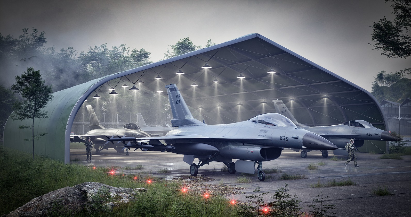 Trzy myśliwce F-16 Fighting Falcon stojące w hangarze z oświetleniem, z żołnierzami w mundurach w pobliżu, w tle zalesiony teren.