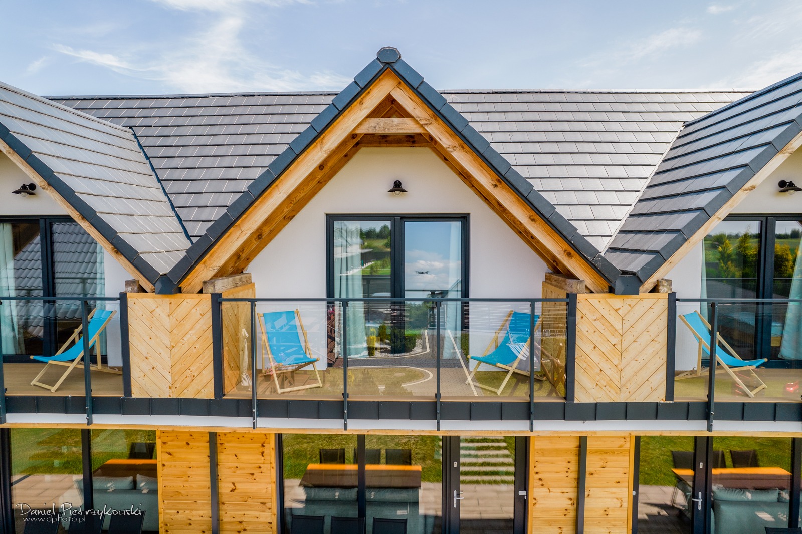 Nowoczesny dom z drewnianymi elementami konstrukcyjnymi, balkonami z niebieskimi leżakami i szklanymi balustradami, widok z góry.