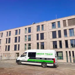 Budynek mieszkalny z jasnej cegły z zamontowanymi oknami i żaluzjami fasadowymi, na pierwszym planie samochód dostawczy firmy DEKOR TEAM.