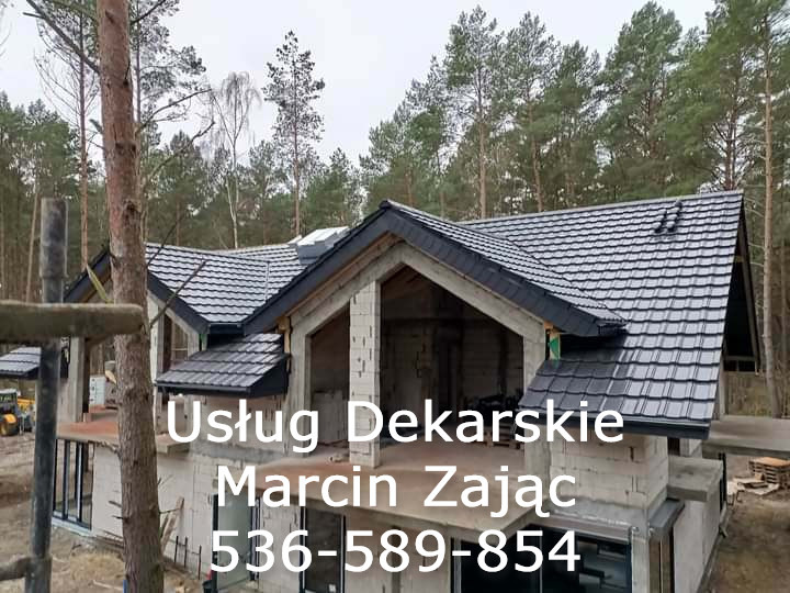 Nowy, czarny dach z blachodachówki na surowym budynku w lesie, widoczne rynny i obróbki blacharskie, w tle drzewa iglaste.