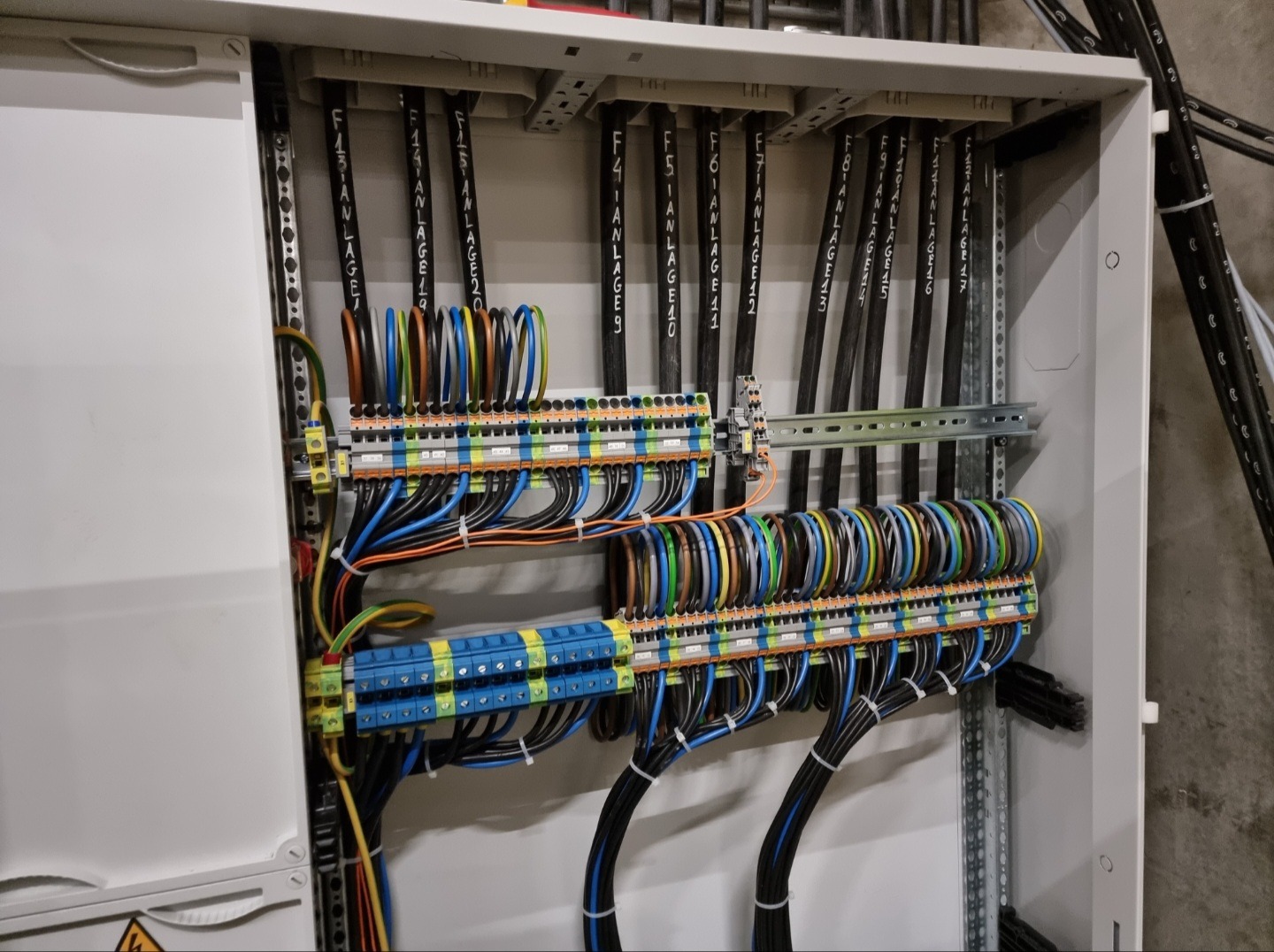 Rozdzielnica elektryczna z precyzyjnie ułożonymi przewodami oznaczonymi numerami instalacji, widoczne listwy zaciskowe i szyny montażowe.