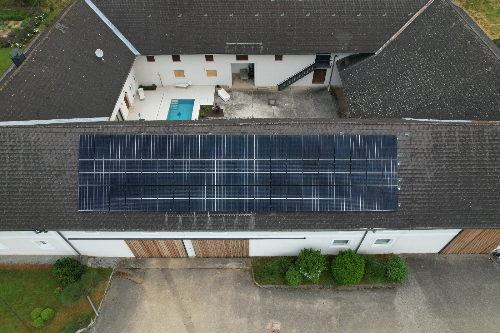Widok z góry na duży budynek gospodarczy z zainstalowanymi panelami słonecznymi na dachu; w tle dziedziniec z basenem.