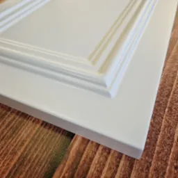 Biały, frezowany front meblowy z płyty MDF, leżący na drewnopodobnym blacie, prezentowany pod kątem.