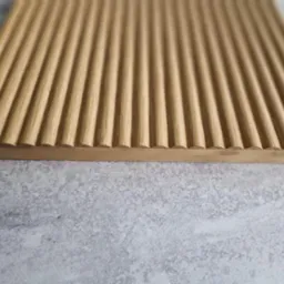 Drewniany blat z równoległymi, zaokrąglonymi żłobieniami, ukazujący naturalne usłojenie drewna na tle szarej, teksturowanej powierzchni.