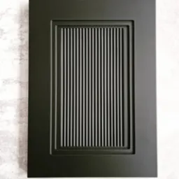 Matowa, czarna frontowa płyta meblowa z frezowanymi, pionowymi żłobieniami w prostokątnej ramce, na tle szarej ściany.