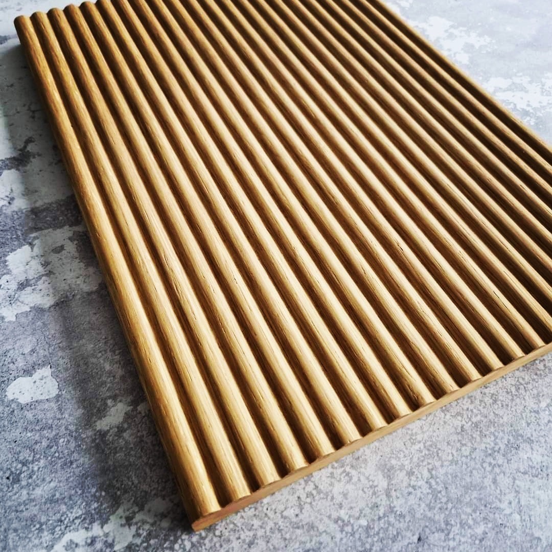 Panel ścienny z drewna z wyraźnymi, równoległymi żłobieniami, ułożony ukośnie na szarej, teksturowanej powierzchni.