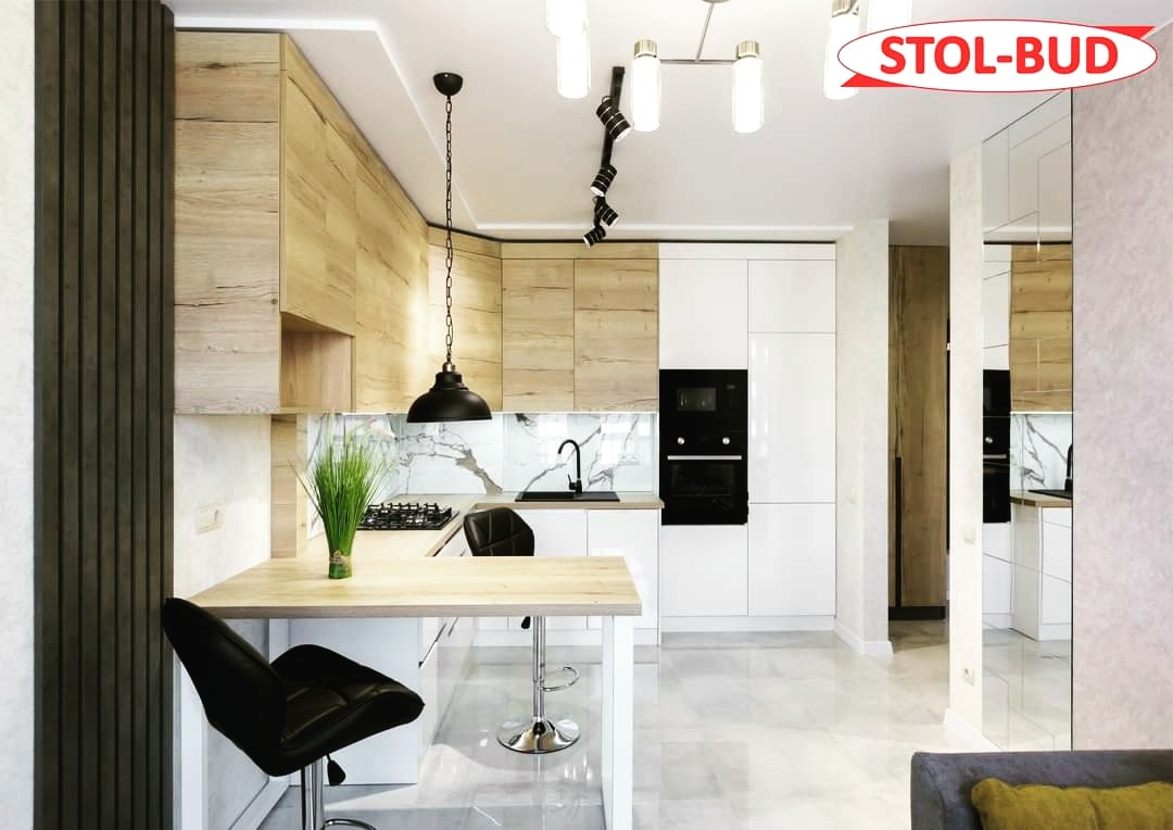 Nowoczesna kuchnia z drewnianymi frontami szafek górnych, białymi frontami dolnych, marmurowym backsplashiem i czarną armaturą, oświetlona lampami wiszącymi i punktowymi, z logo firmy w prawym...