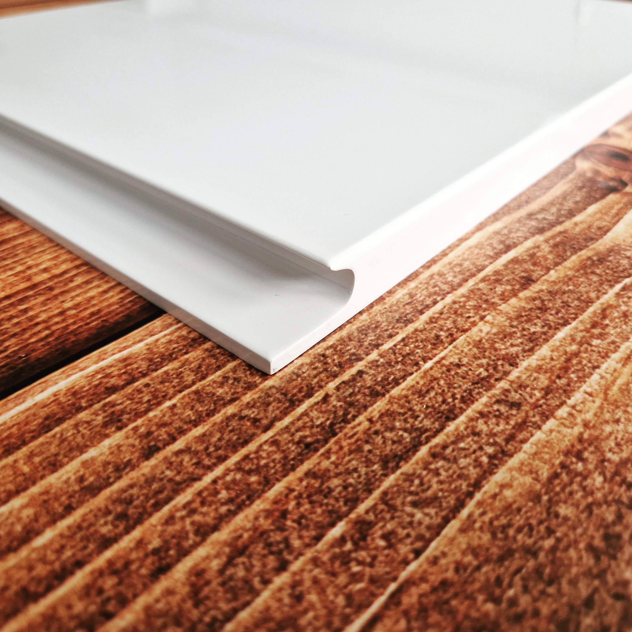 Detalle de canto de puerta o cajón blanco sobre superficie de madera con veta pronunciada.