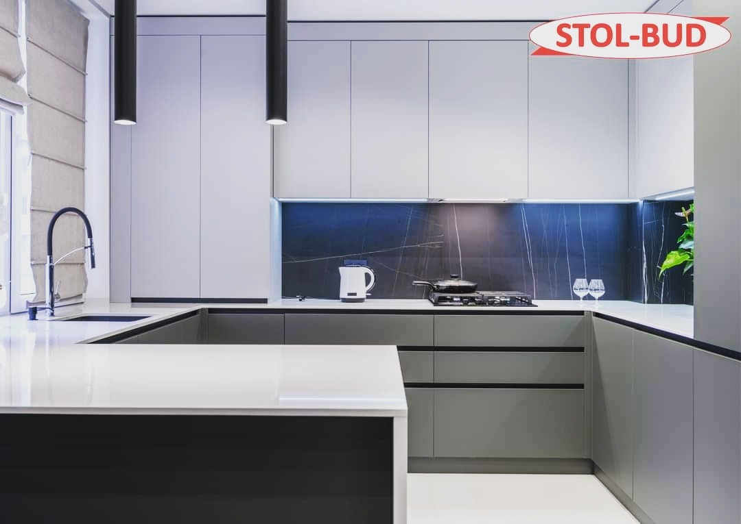 Nowoczesna kuchnia w odcieniach szarości z wyspą, oświetleniem punktowym i marmurowym backsplash'em, uzupełniona logiem firmy STOL-BUD w prawym górnym rogu.