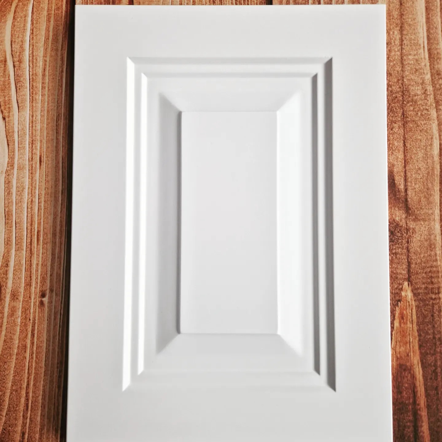 Biały, frezowany front meblowy z płyty MDF, leżący na blacie z naturalnego drewna.