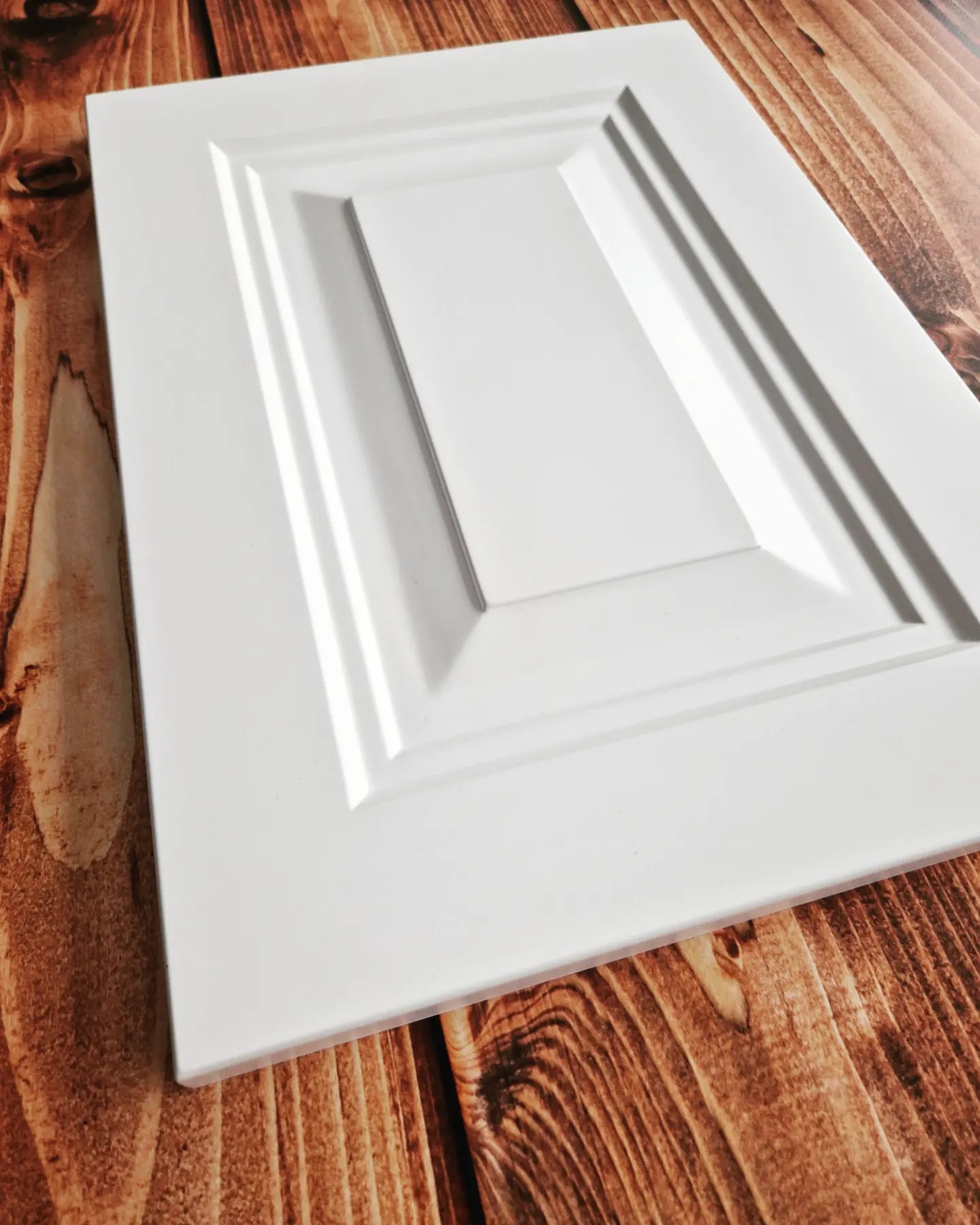 Biały front meblowy z frezowanym wzorem, prezentowany przez stolarza z Rybna na tle blatu z ciemnego drewna.