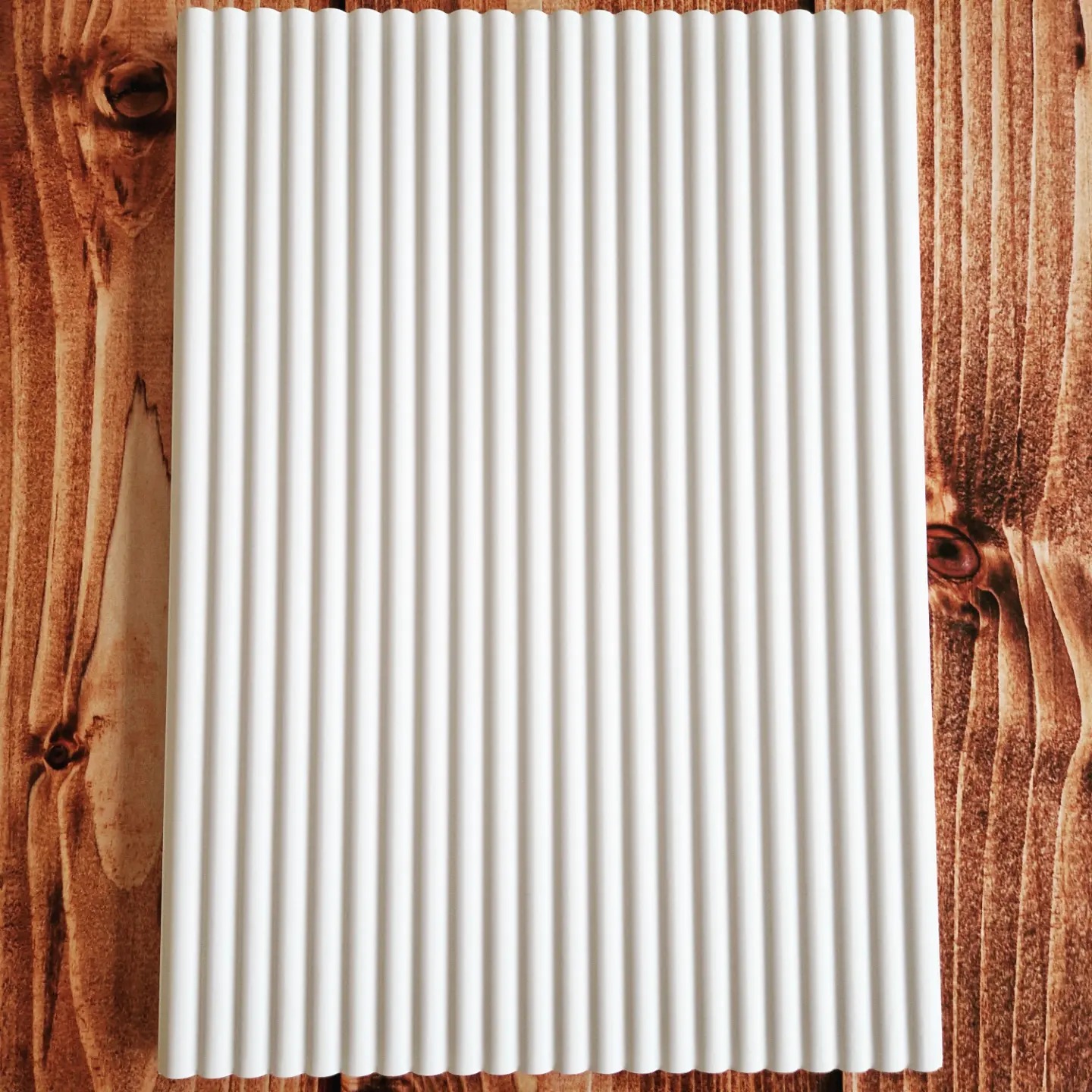 Biały, ryflowany panel na tle rustykalnej, drewnianej deski.