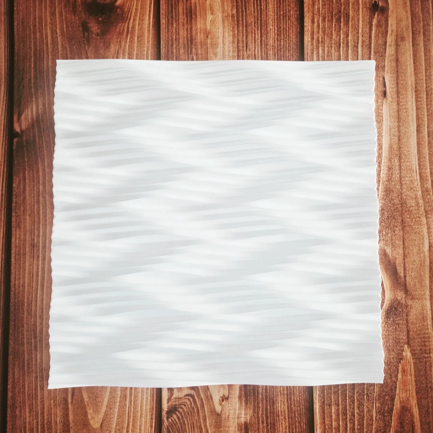 Arkusz białego, karbowanego materiału leży na blacie z ciemnego drewna z wyraźnym usłojeniem.