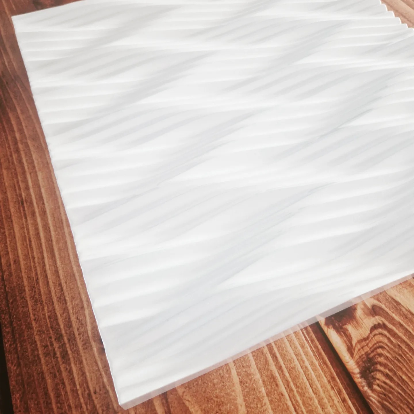 Biały, falisty panel dekoracyjny na tle drewnianego blatu o wyraźnym usłojeniu.