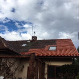 Mycie ciśnieniowe - Częściowo wyczyszczony czerwony dach z dachówki ceramicznej na tle pochmurnego nieba, widoczny kontrast między czystą a zabrudzoną powierzchnią dachu.