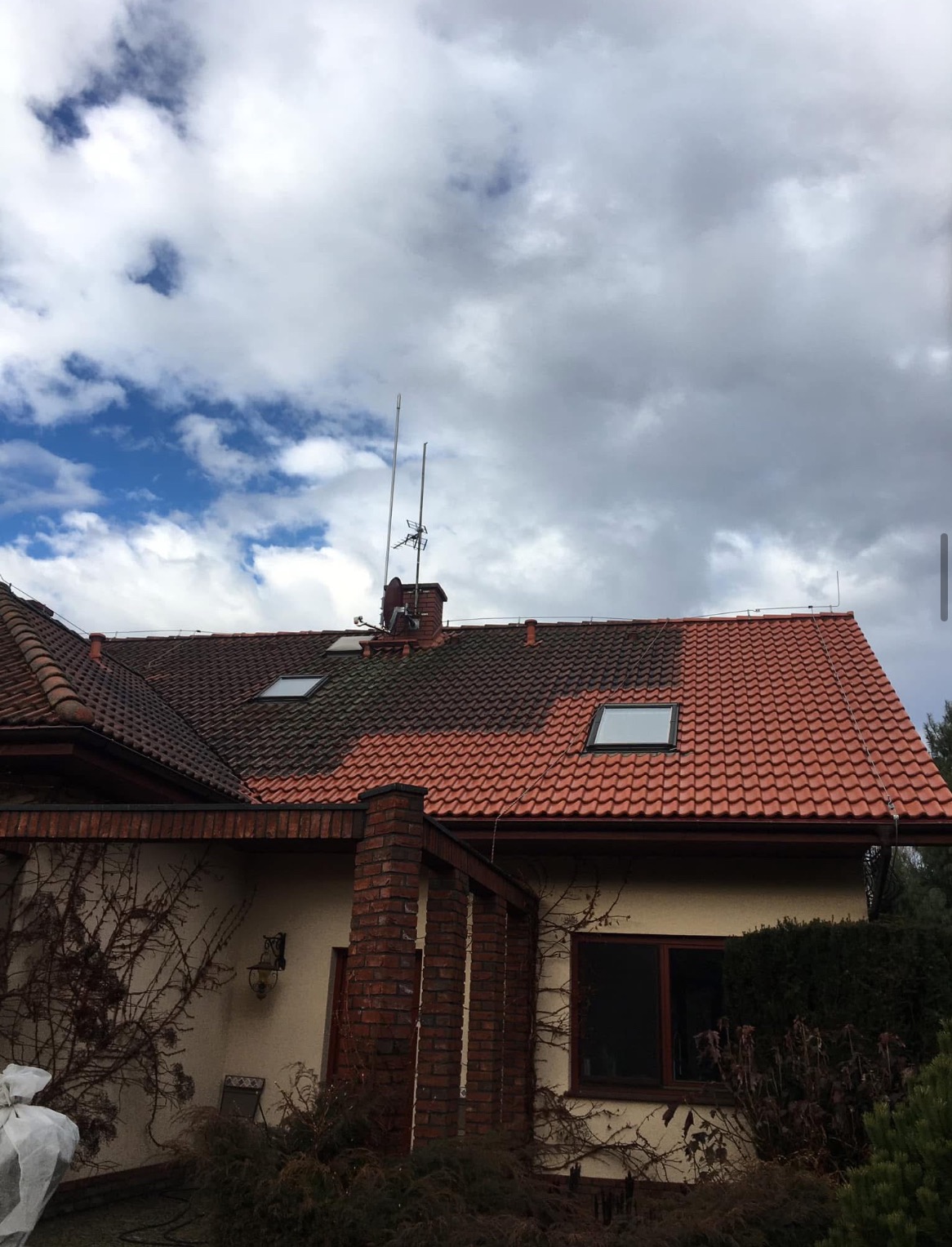Częściowo wyczyszczony czerwony dach z dachówki ceramicznej na tle pochmurnego nieba, widoczny kontrast między czystą a zabrudzoną powierzchnią dachu.