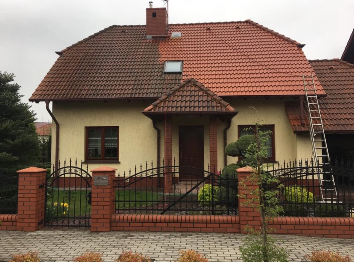 Dom jednorodzinny z częściowo wyczyszczonym dachem z czerwonej dachówki, widoczna różnica w kolorze między czystą a zabrudzoną powierzchnią, drabina oparta o ścianę.