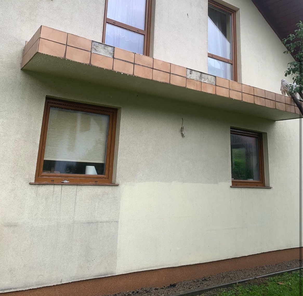 Fragment elewacji budynku z widocznym obszarem po czyszczeniu, kontrastującym z zabrudzoną powierzchnią, oraz uszkodzonymi płytkami pod okapem.