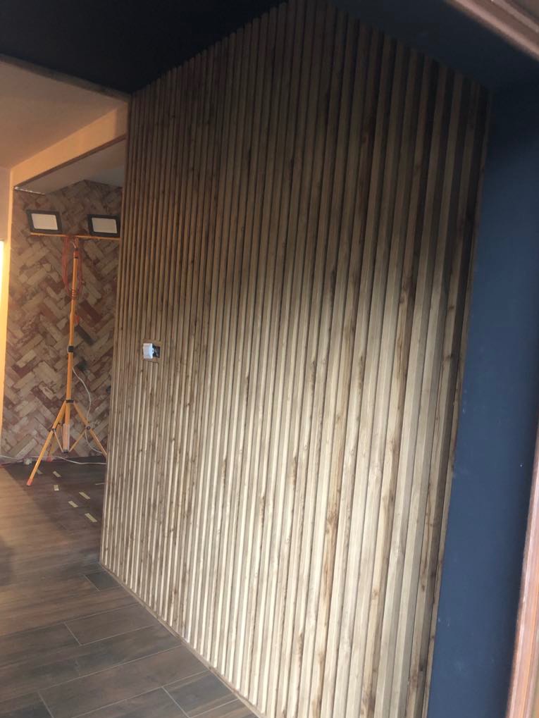 Ściana wykończona drewnianymi lamelami w pionowym układzie, oświetlona lampami budowlanymi, z widoczną instalacją elektryczną. Nowoczesny design wnętrza.