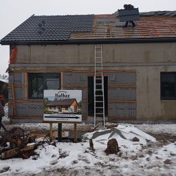 Oleksandr Vasiliev DACHOLEK - Układanie blachodachówki na dachu domu w Poznaniu. Widoczna drabina oparta o budynek i częściowo pokryty dach. Na pierwszym planie tablica informacyjna.