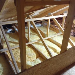 Oleksandr Vasiliev DACHOLEK - Ocieplone wełną mineralną poddasze z drewnianą konstrukcją więźby dachowej. Widok z dołu, fragment płyty OSB w rogu kadru.