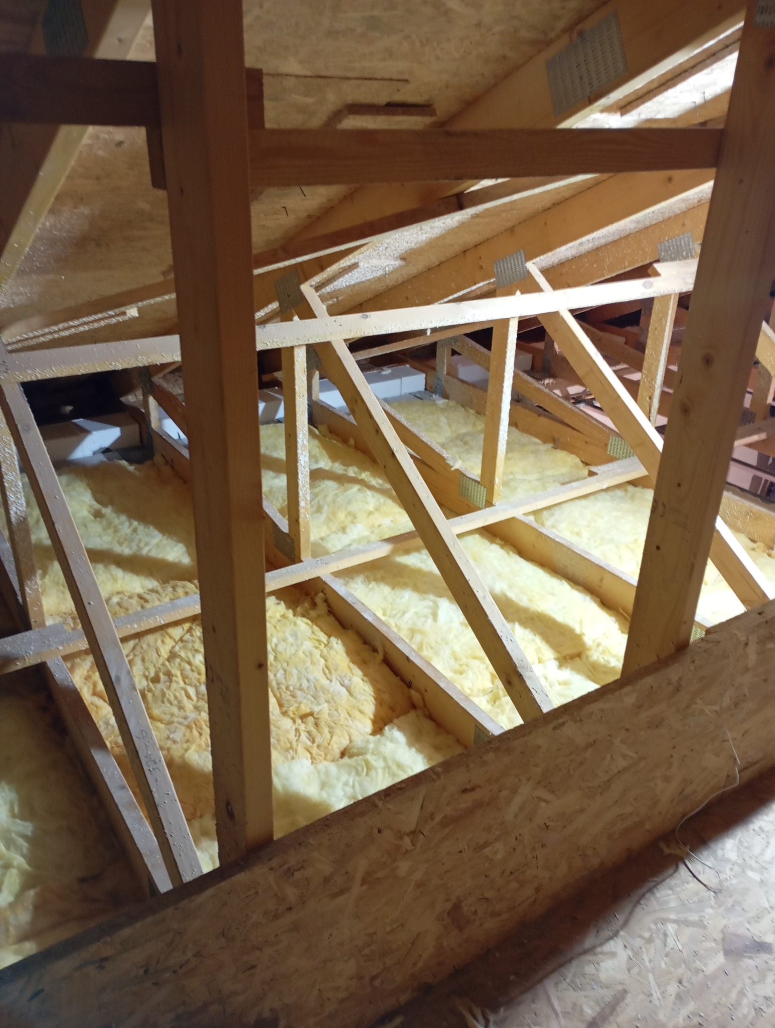 Ocieplone wełną mineralną poddasze z drewnianą konstrukcją więźby dachowej. Widok z dołu, fragment płyty OSB w rogu kadru.