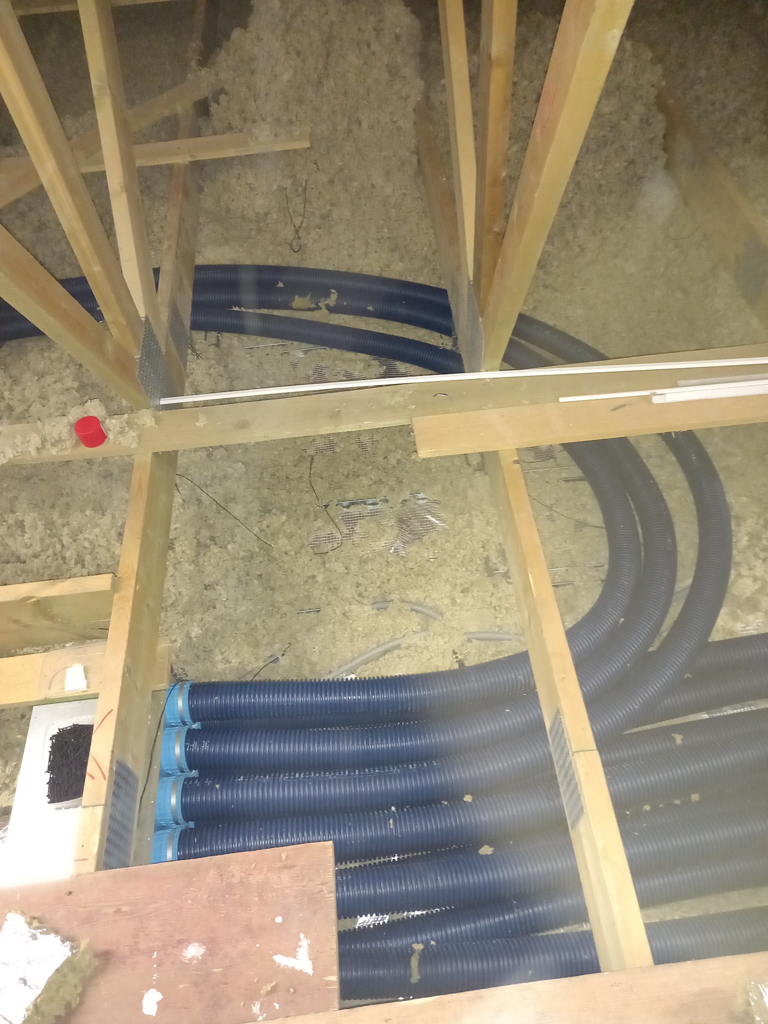 Montaż rur wentylacyjnych w przestrzeni poddasza, widoczne elementy drewnianej konstrukcji dachu i izolacja z wełny mineralnej.