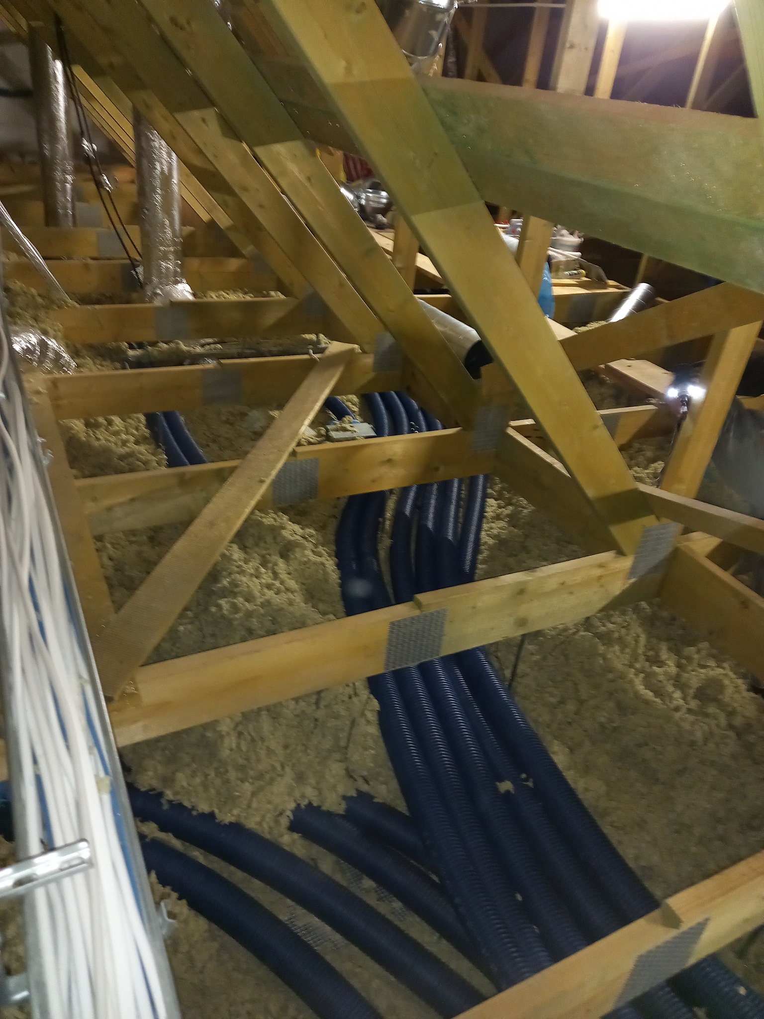 Montaż instalacji rekuperacji w przestrzeni poddasza: widoczne rury wentylacyjne w izolacji, elementy drewnianej konstrukcji dachu oraz przewody elektryczne.