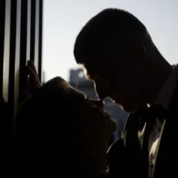 Silhouettes of a bride and groom in a close embrace, captured against a textured wall with natural light highlighting their faces.